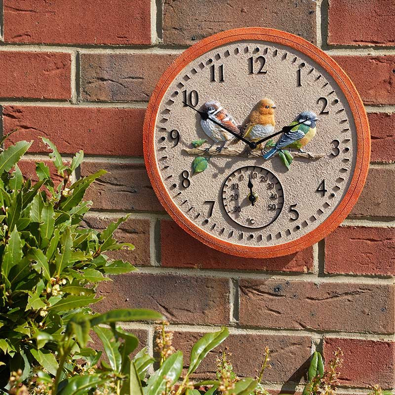 Outdoor wall clock showing built‑in °C thermometer on a brick wall
