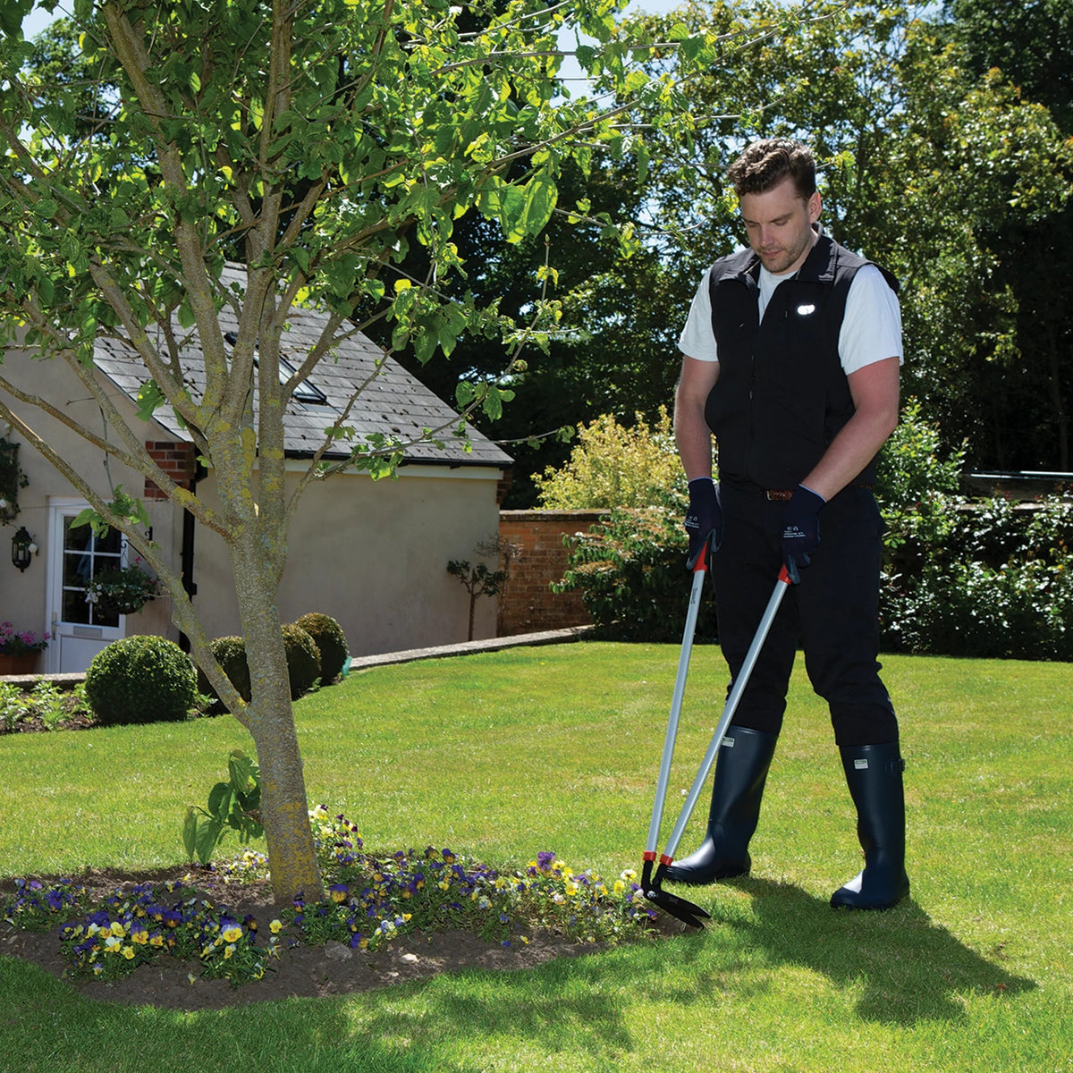 Man gardening using a Wilkinson Sword long reach edging shears for creating neat lawn borders and pathways in a well-maintained lawn with a tree and house in the background