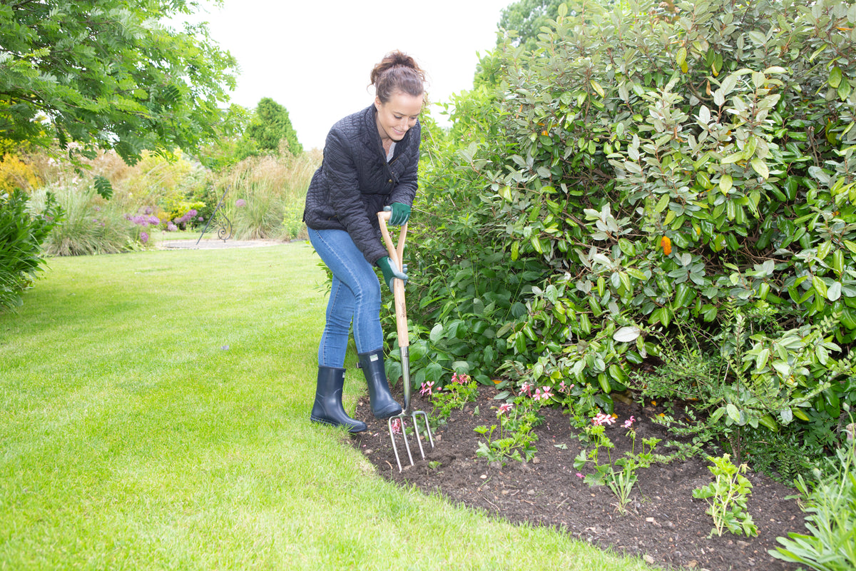 women shown digging in a garden with a Wilkinson Sword Stainless Steel Border Fork with mirror-polished stainless steel head and weatherproof ash handle for cultivating borders and lifting plants