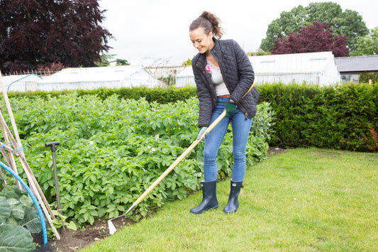 Woman gardening in a lush green garden with plants and a Wilkinson Sword swoe style hoe for precision weeding in flower beds and borders.