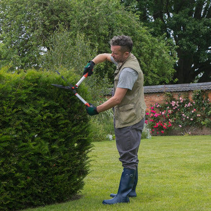 Man trimming a hedge with Wilkinson Sword manual hedge cutter with wavy blades for accurate hedge shaping in a garden setting.